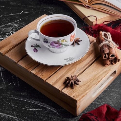 A charming cup of tea with a bundle of cinnamon sticks on a wooden serving board