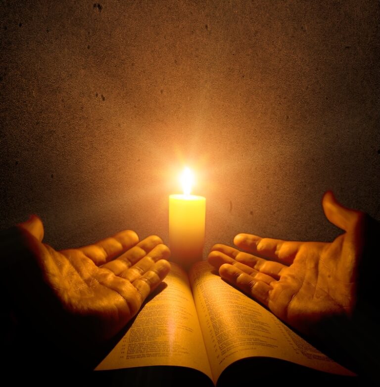 open hands over a bible receiving candle light