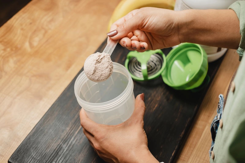 woman scooping protein powder into a shaker cup