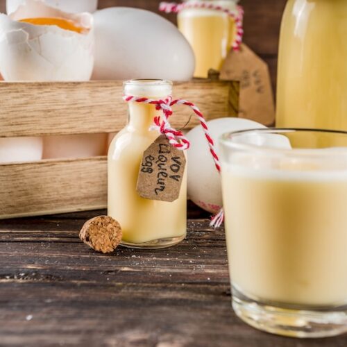 Creamy homemade eggnog in glasses and a corked bottle on a rustic wooden table with fresh eggs
