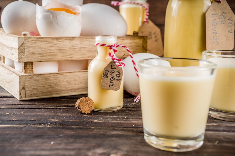 Creamy homemade eggnog in glasses and a corked bottle on a rustic wooden table with fresh eggs