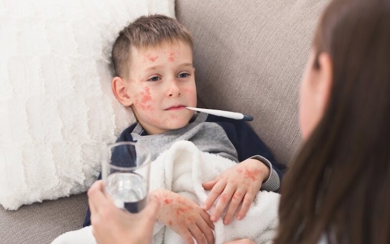 Mother caring for boy with measles at home, checking temperature
